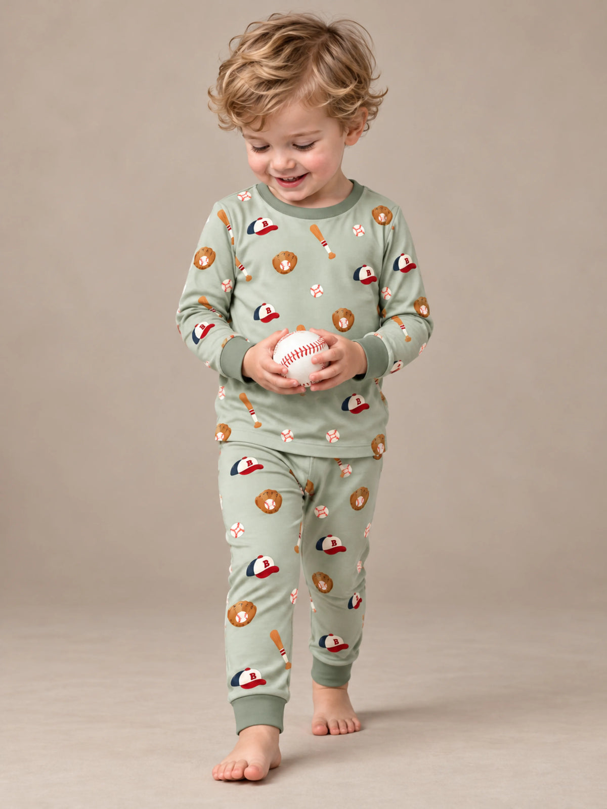 Toddler wearing Little Sluggers sage green bamboo baseball pajamas in a studio