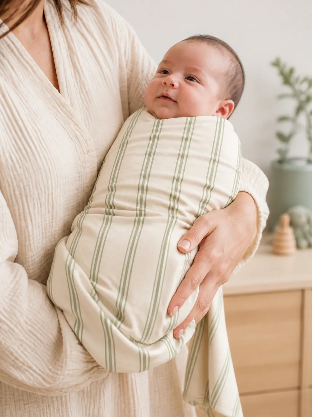 Baby cuddled in the Sage Stripe bamboo swaddle blanket at home