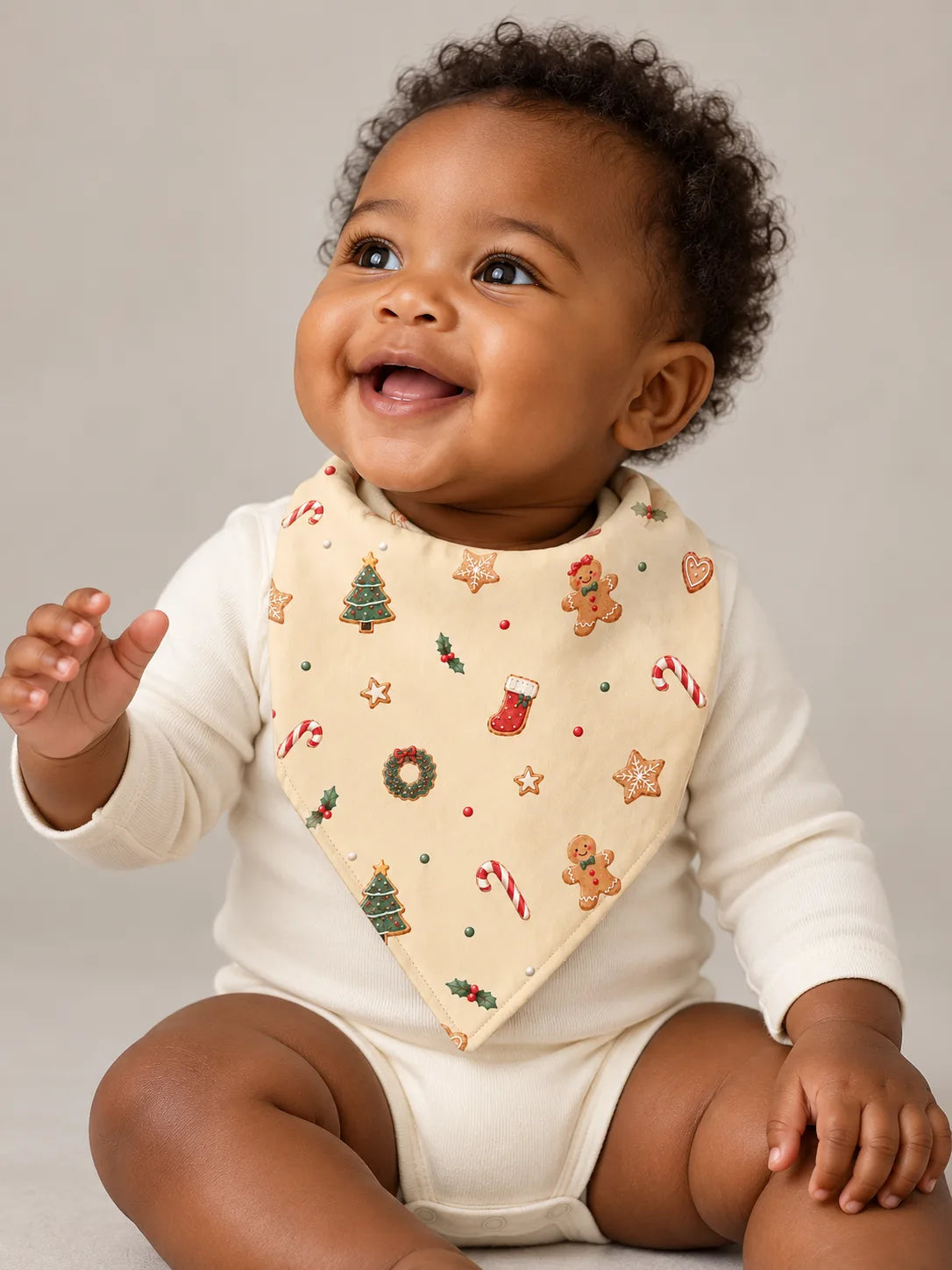 Smiling baby wearing the MossiBaby Christmas Joy bandana bib over an ivory bodysuit in a studio.