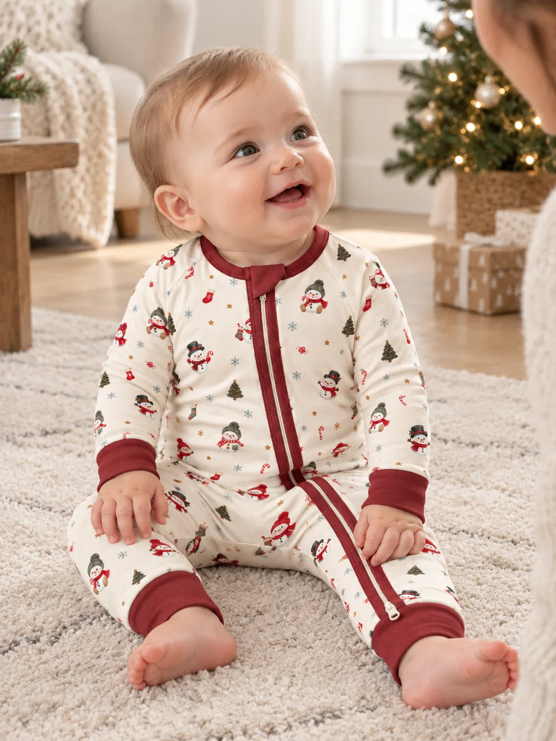 Baby sitting by a Christmas tree at home wearing Mossibaby Christmas Snowman ivory cream bamboo zipper romper with cranberry red trim