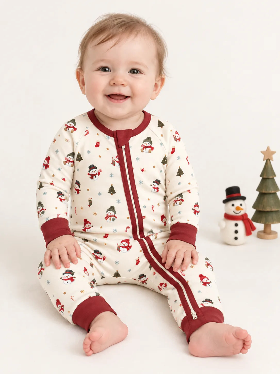 Baby sitting in a studio wearing Mossibaby Christmas Snowman ivory cream bamboo zipper romper with cranberry red trim
