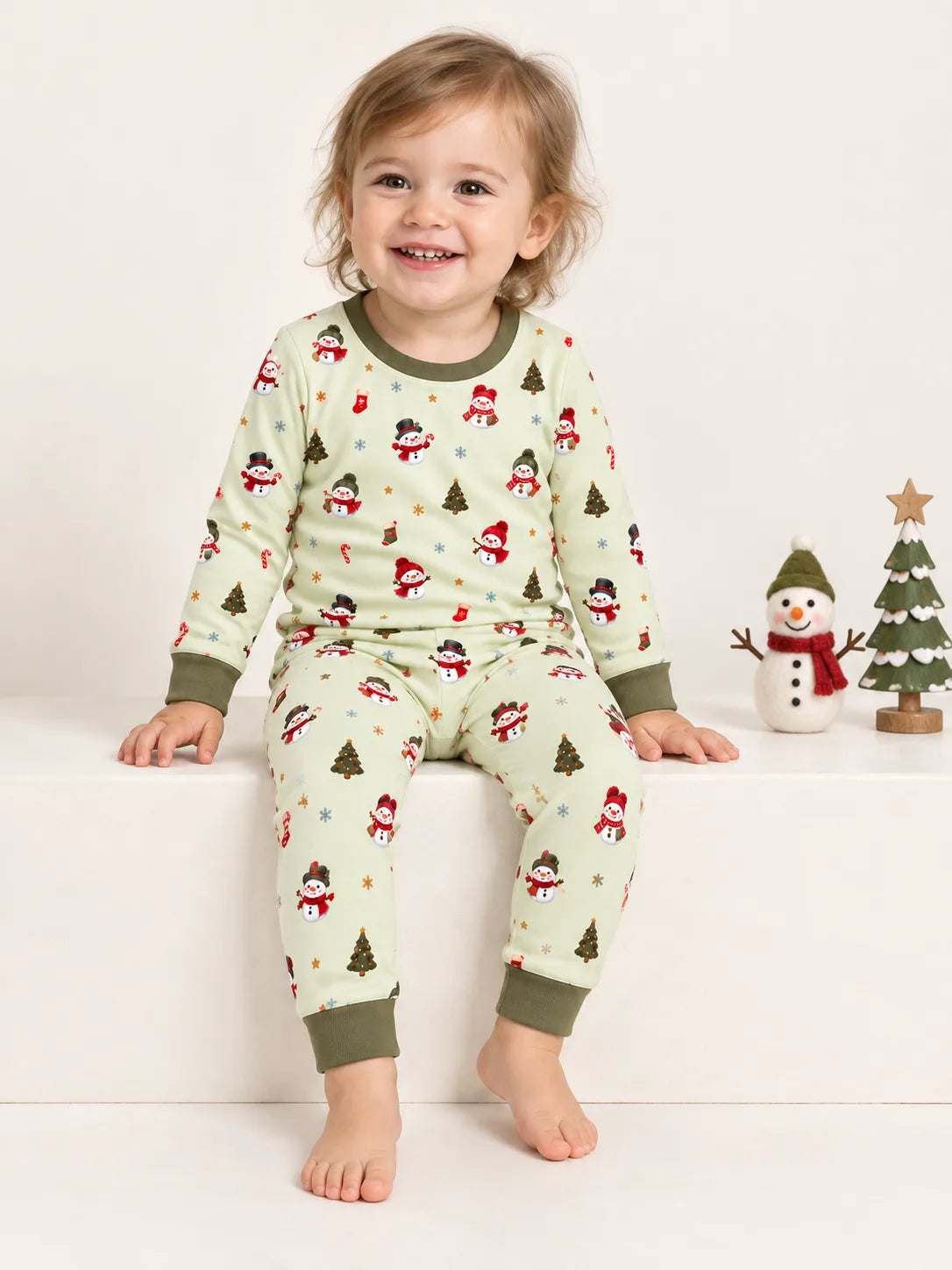 Toddler sitting in a studio wearing Mossibaby Christmas Snowman pale green bamboo long sleeve pajama set with olive green trim