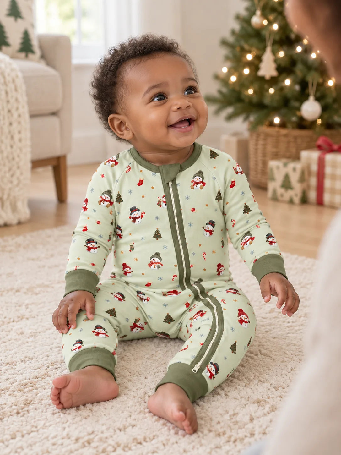Baby sitting by a Christmas tree at home wearing Mossibaby Christmas Snowman pale green bamboo zipper romper with olive green trim