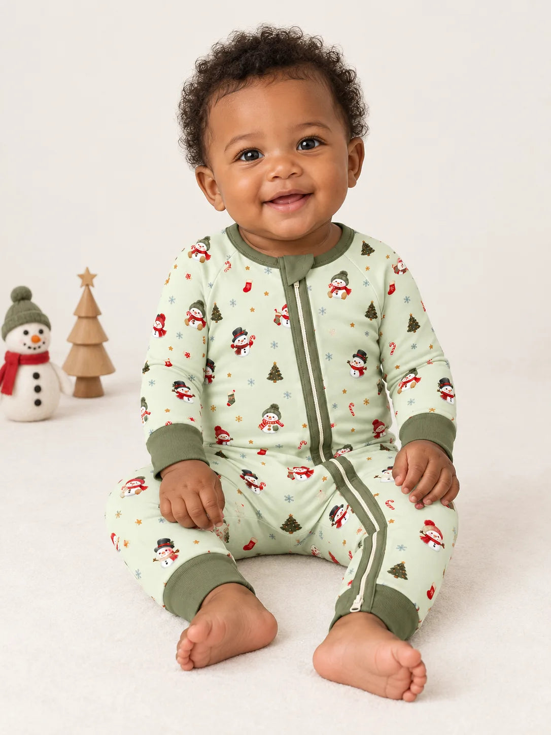 Baby sitting in a studio wearing Mossibaby Christmas Snowman pale green bamboo zipper romper with olive green trim