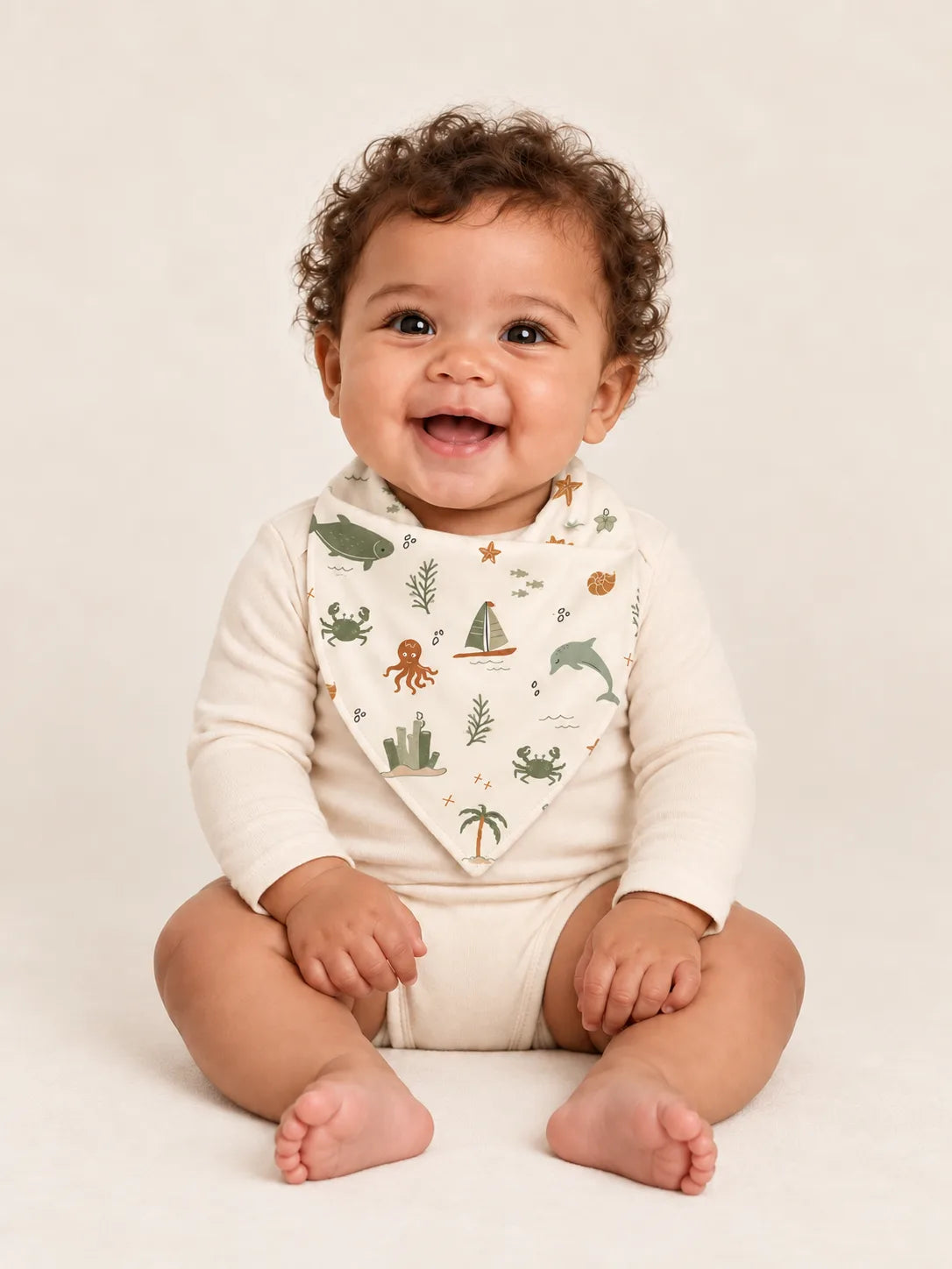 Baby wearing the MossiBaby Coastal Friends bandana bib with an ivory long-sleeve bodysuit