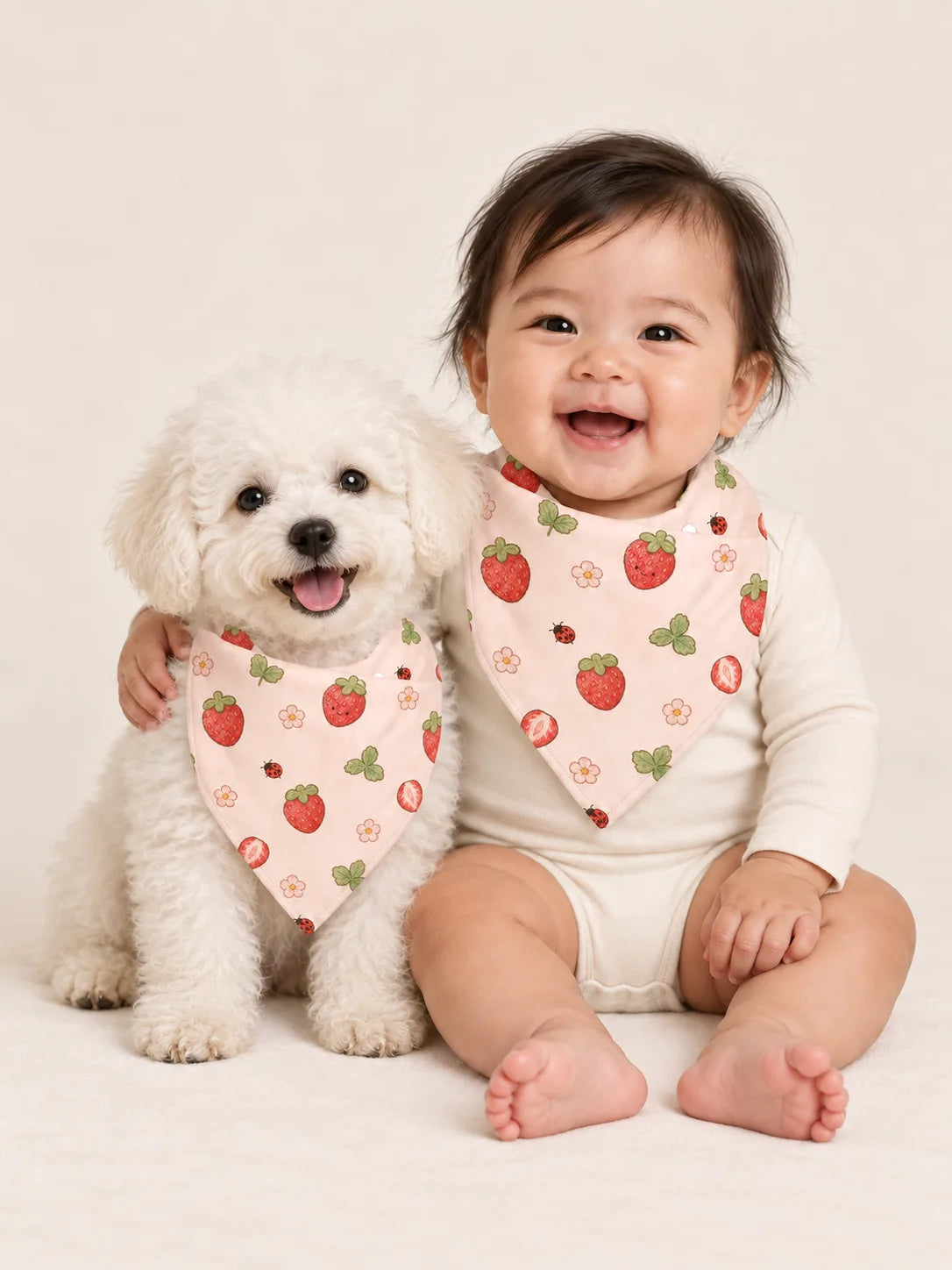 Baby and Bichon Frise puppy wearing matching MossiBaby Strawberry Fields bandana bibs
