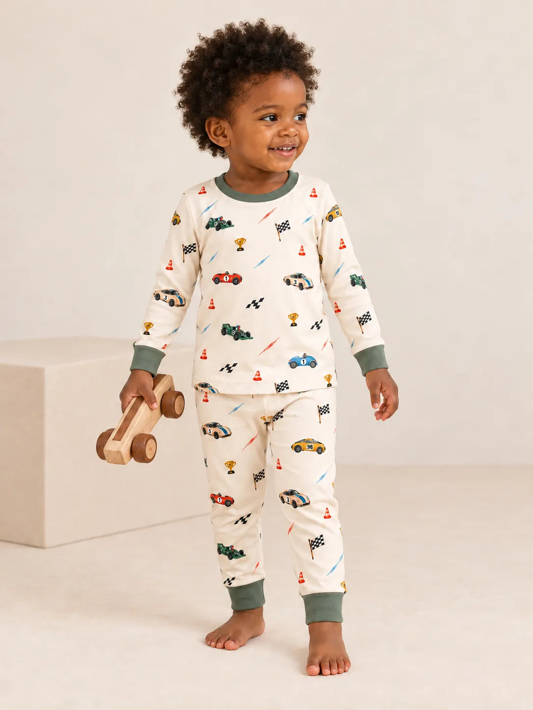 Child standing in the Vintage Racers bamboo pajama set while holding a wooden racing car in a studio.