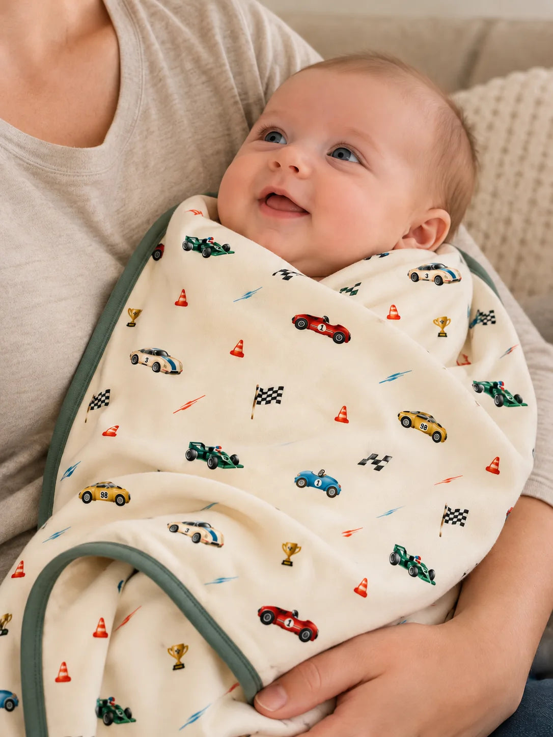 Baby cradled in a parent's arms in the Vintage Racers bamboo baby blanket, with its green edge visible.