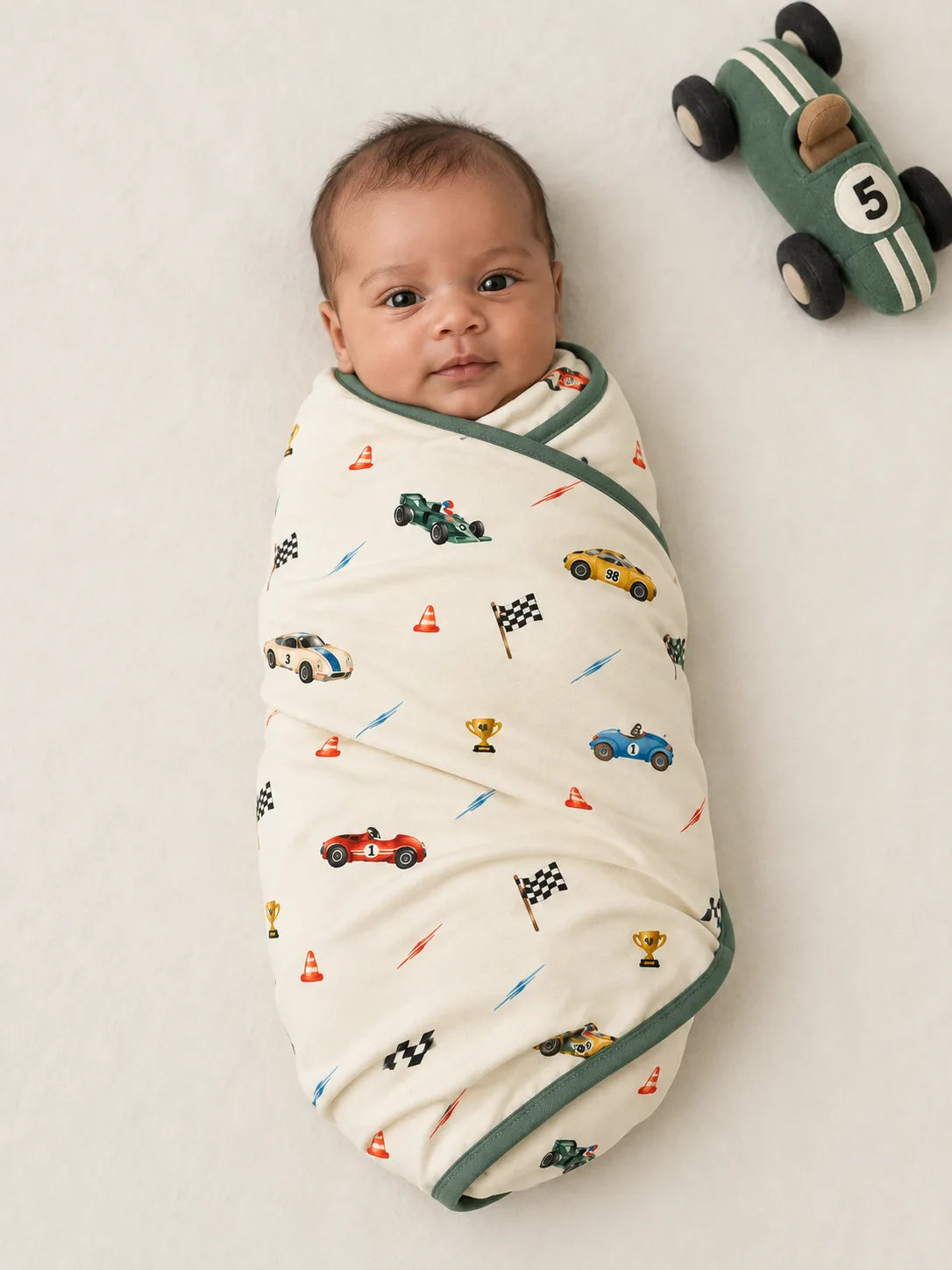 Baby wrapped in the Vintage Racers bamboo baby blanket with green binding in an overhead studio photo.