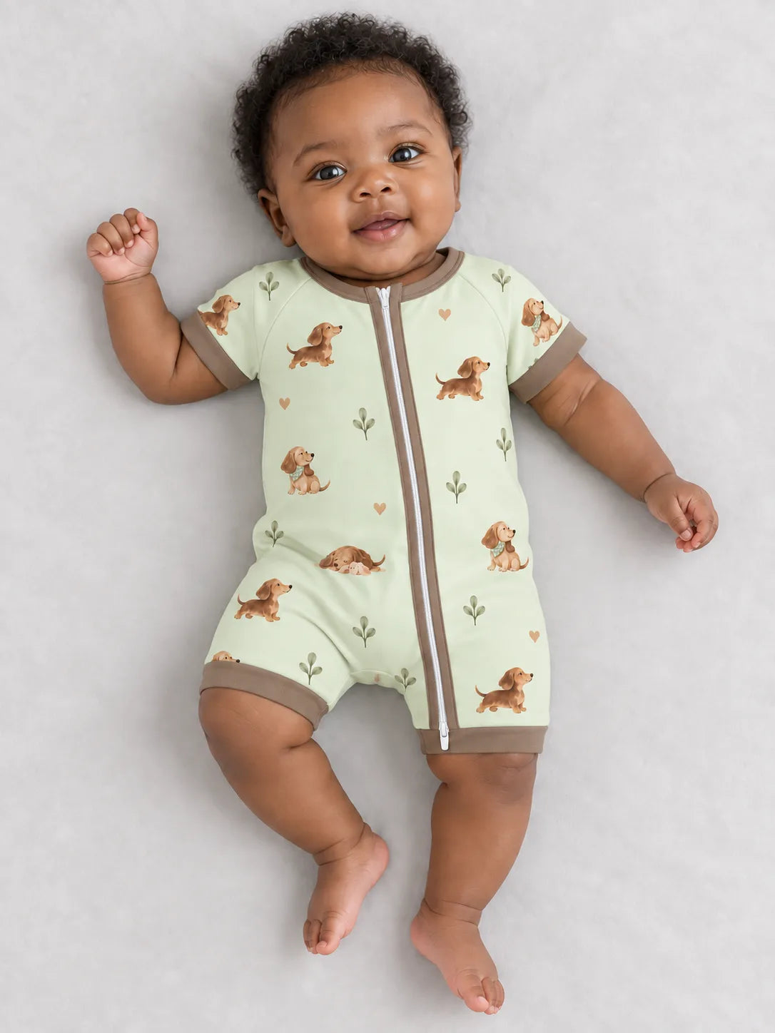 Baby wearing the MossiBaby dachshund meadow shorty romper against a pale studio backdrop