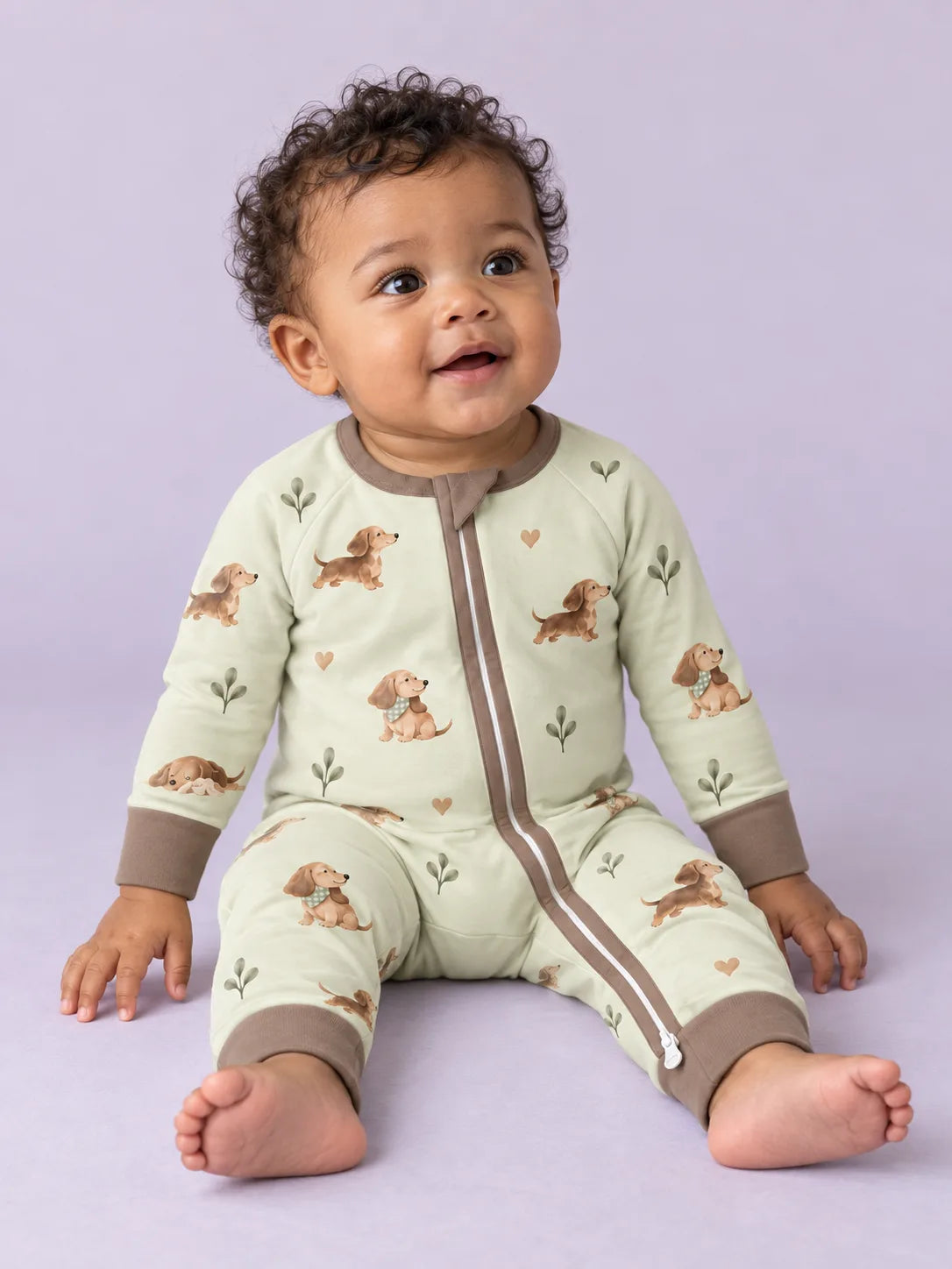 Baby wearing the MossiBaby dachshund meadow zipper romper against a pale studio backdrop