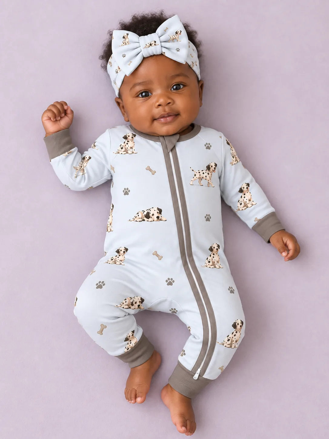 Baby wearing the MossiBaby Dalmatian Days bow headband with a matching zipper romper against a pale studio backdrop