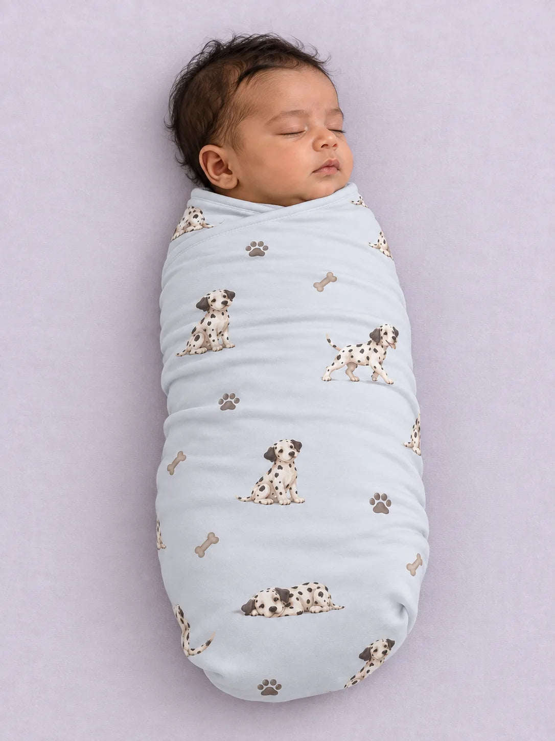 Baby wrapped in the MossiBaby dalmatian days swaddle blanket against a pale studio backdrop