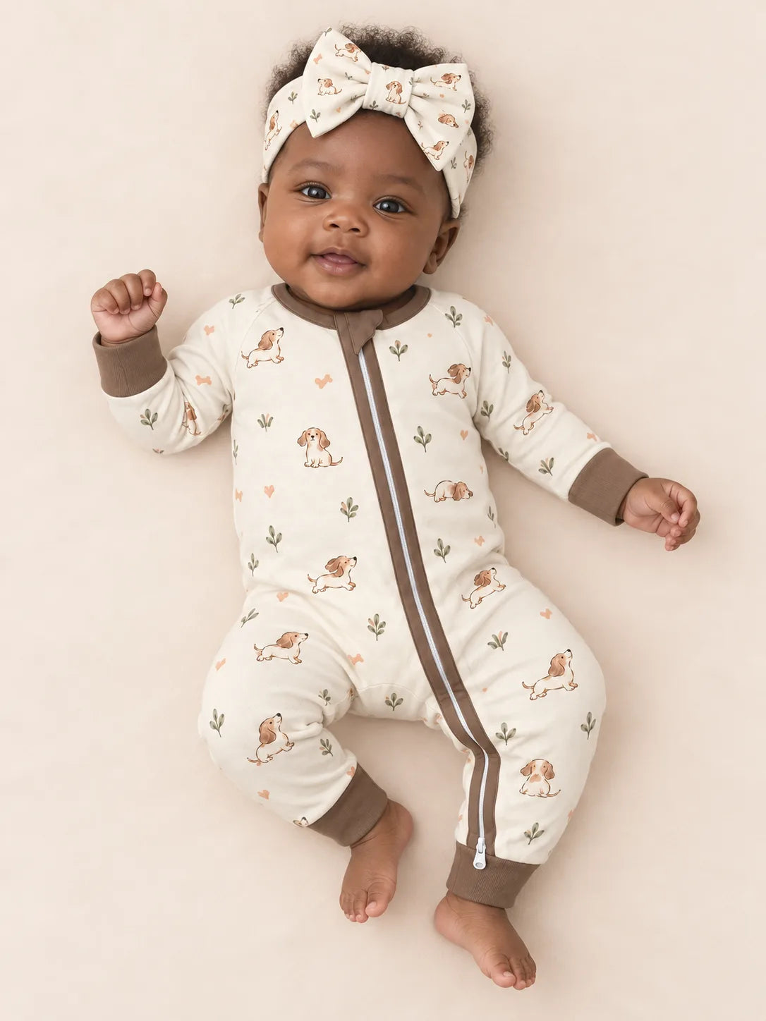 Baby wearing the MossiBaby Doxie Dreams bow headband with a matching zipper romper against a pale studio backdrop