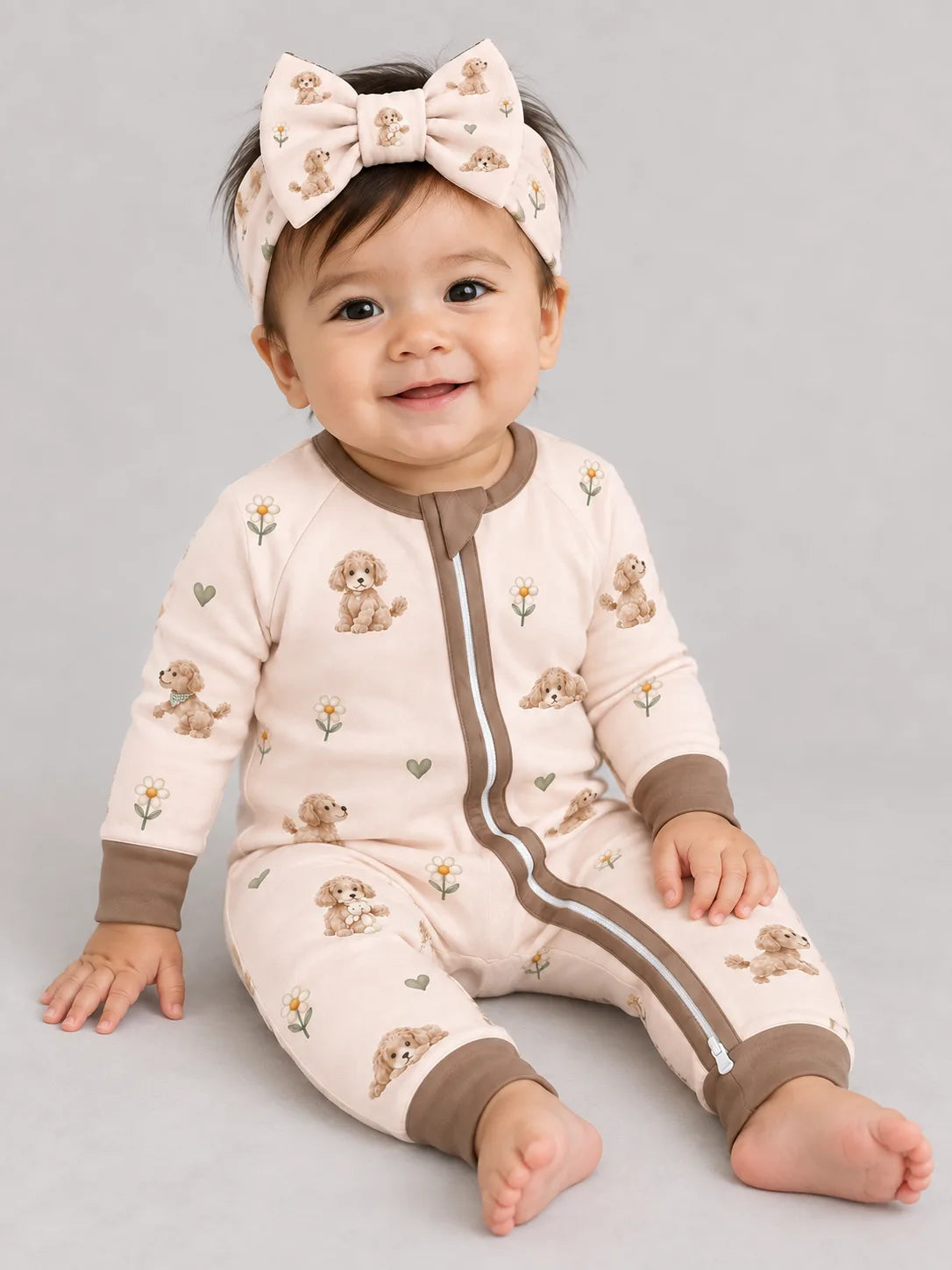 Baby wearing the MossiBaby Poodle Petals bow headband with a matching zipper romper against a pale studio backdrop
