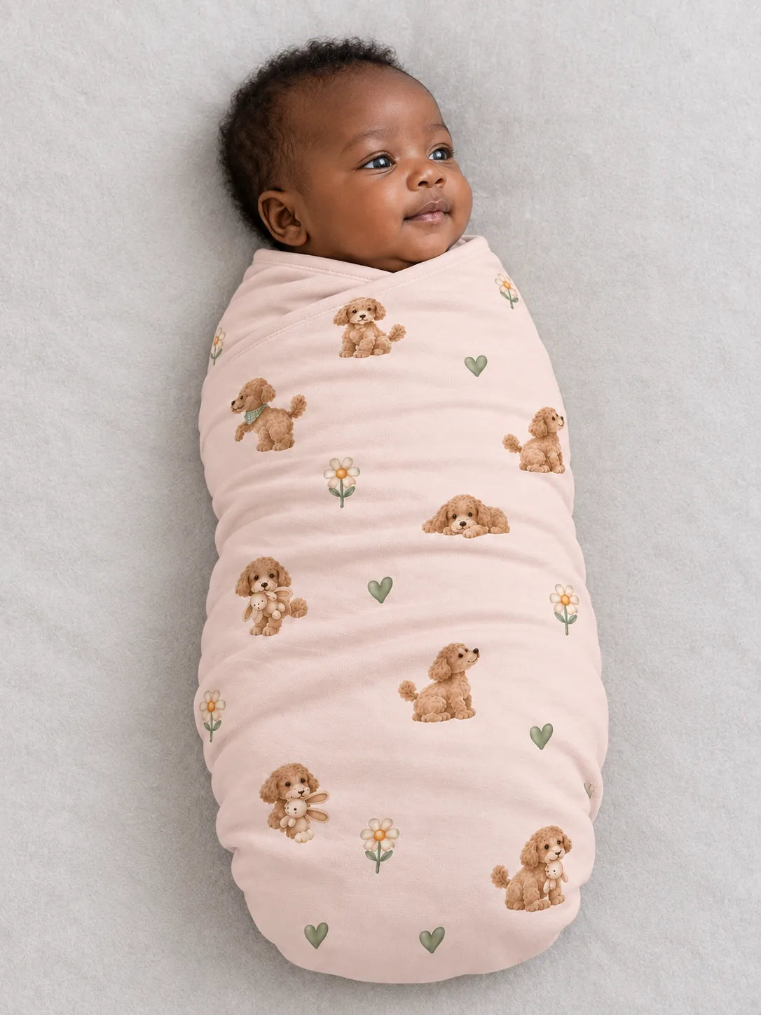 Baby wrapped in the MossiBaby poodle petals swaddle blanket against a pale studio backdrop