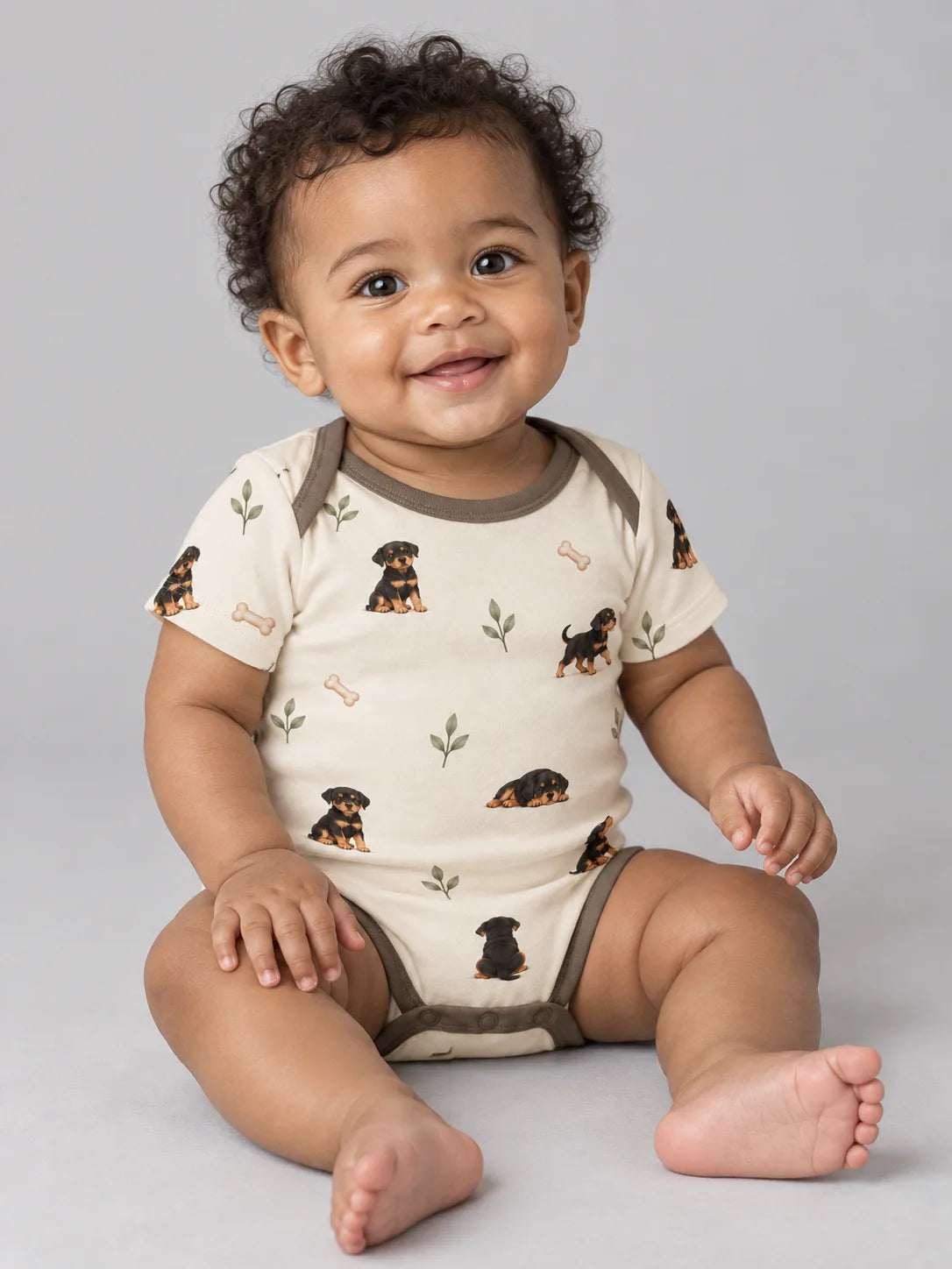 Baby wearing the MossiBaby rottie cuddles short sleeve bodysuit against a pale studio backdrop