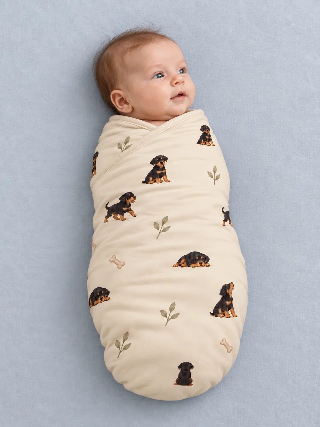 Baby wrapped in the MossiBaby rottie cuddles swaddle blanket against a pale studio backdrop